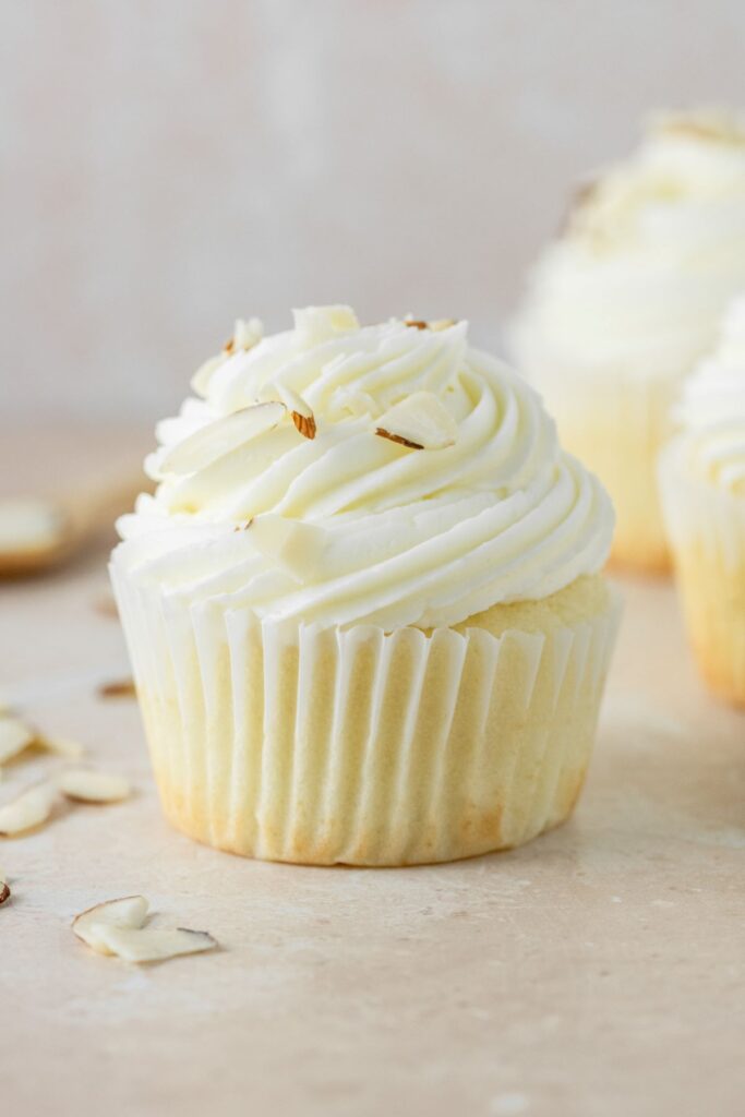 A close up of an almond cupcake that's topped with almond frosting and thinly sliced almond pieces.