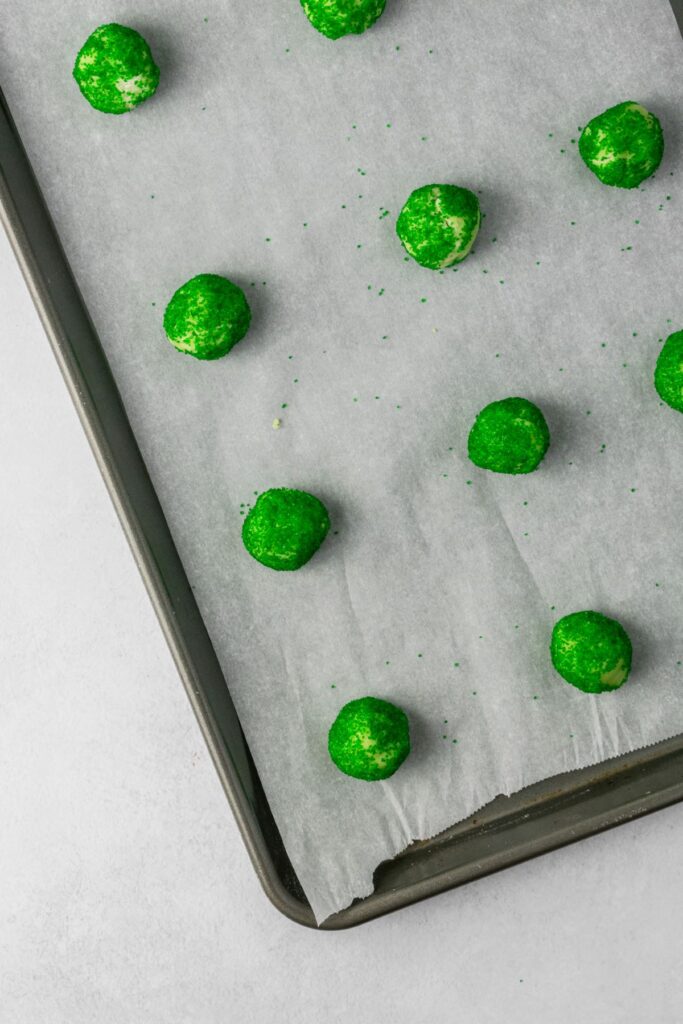 Cookie dough balls rolled in green sugar placed on a parchment paper lined baking sheet.
