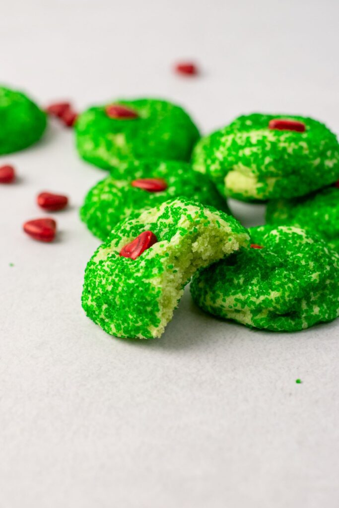 A bite taken out of a green Christmas sugar cookie. Each cookie has a red heart sprinkle.