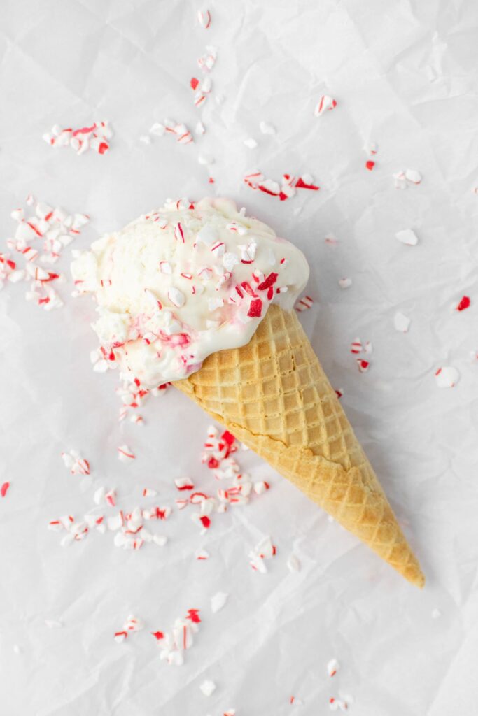 Peppermint candy cane ice cream cone with candy pieces all around it.