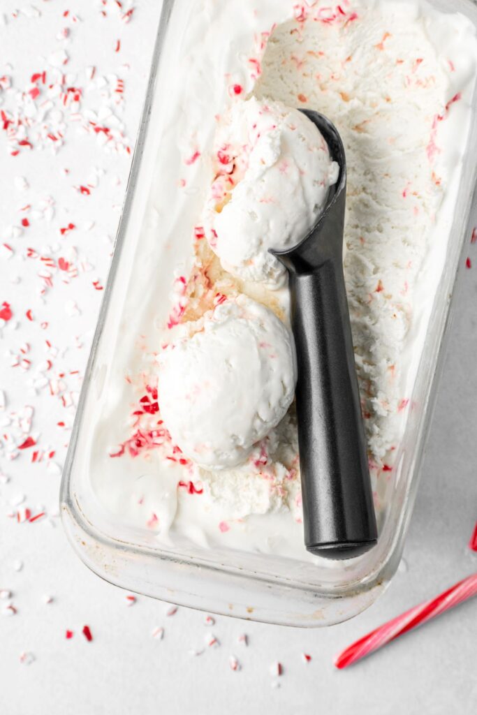 Candy cane ice cream recipe with an ice cream scoop in the pan. It's covered in crushed candy cane pieces.