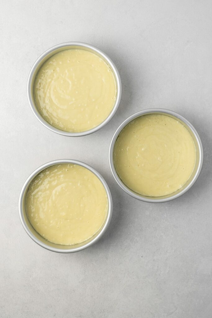 Three six inch cake pans filled with cake batter.
