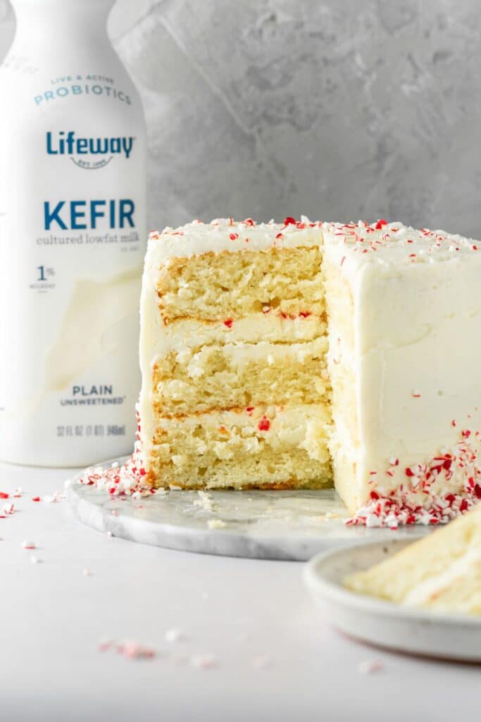 A three layer holiday cake with peppermint candies on the outside and a bottle of kefir off to the side.