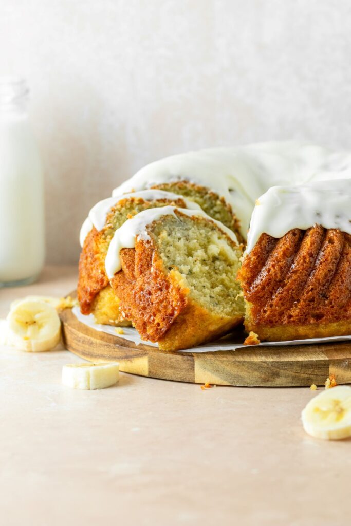 Banana bundt cake with a cream cheese glaze on top. There are banana slices and a jar of milk off to the side.