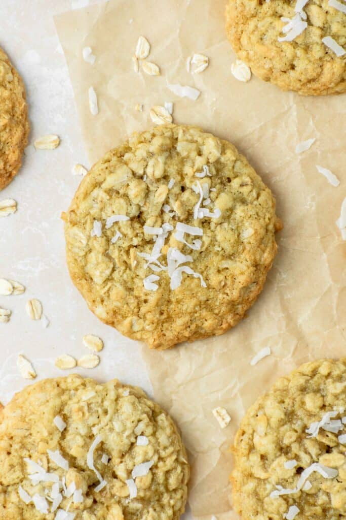 A chewy oatmeal coconut cookie sitting on brown parchment paper with coconut flakes all over.