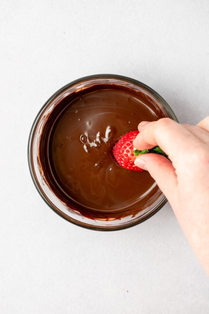 Dipping a strawberry into melted dark chocolate.
