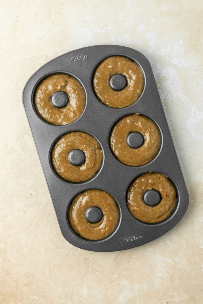 A six cup donut pan filled with batter ready to bake.