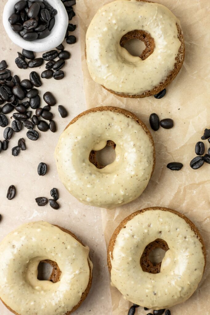 Coffee baked donuts on brown parchment paper with espresso beans laying off to the side.