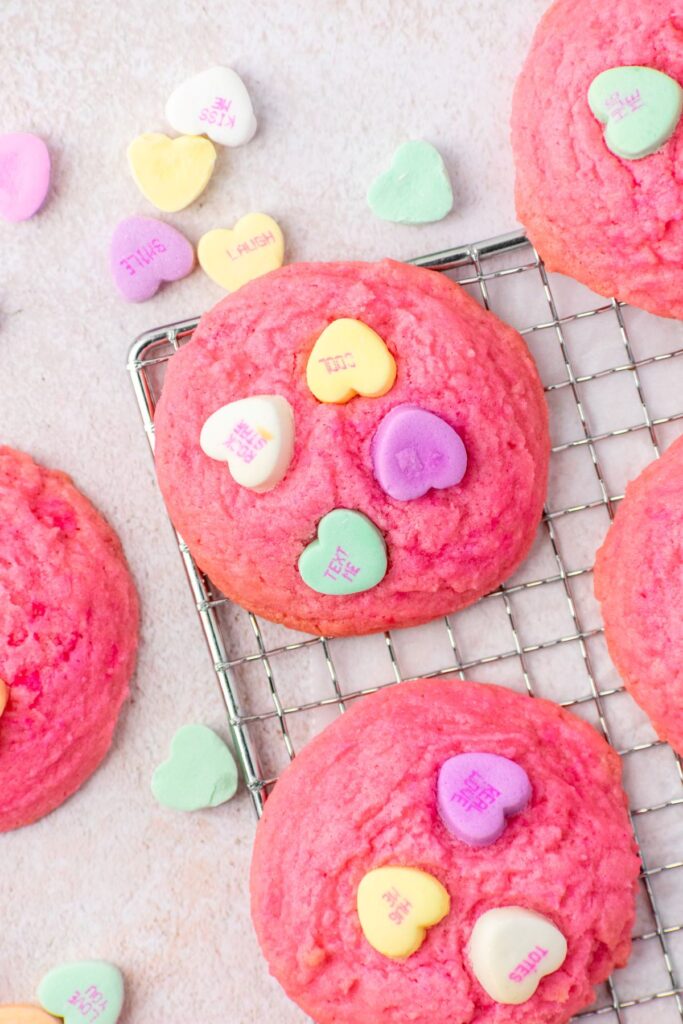 Valentine's Day sugar cookies on a wire rack with little conversation hearts on top.