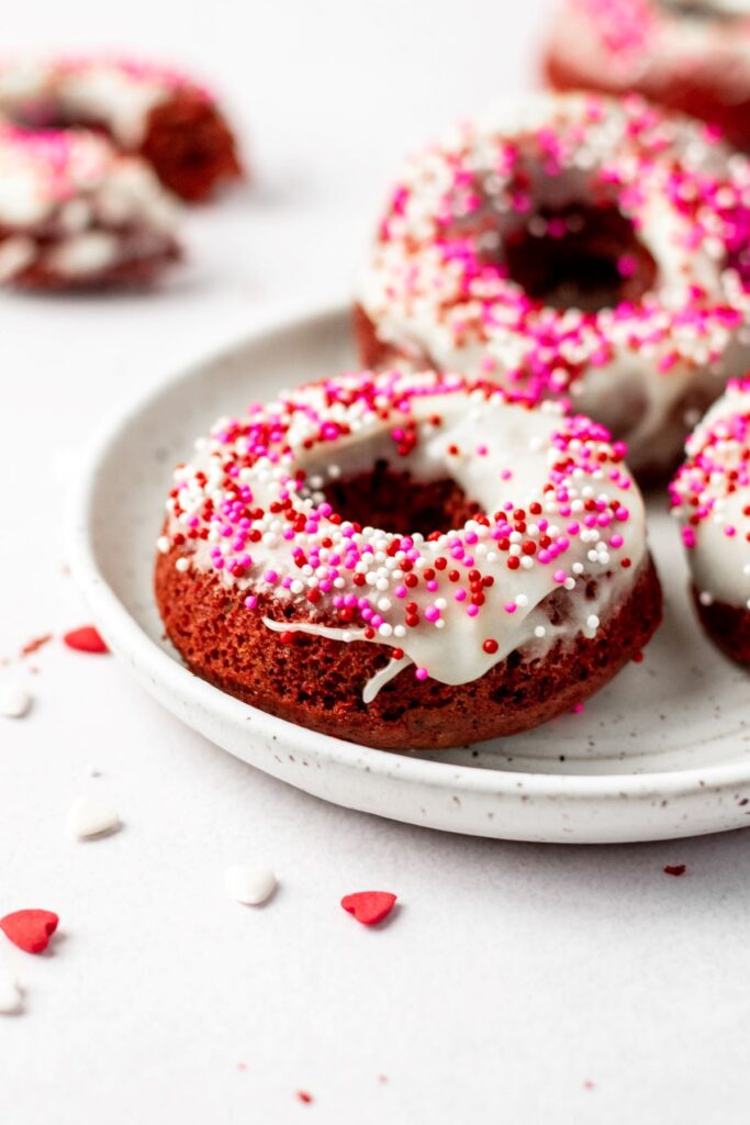 Baked red velvet donuts covered in sprinkles and sitting on a white plate.
