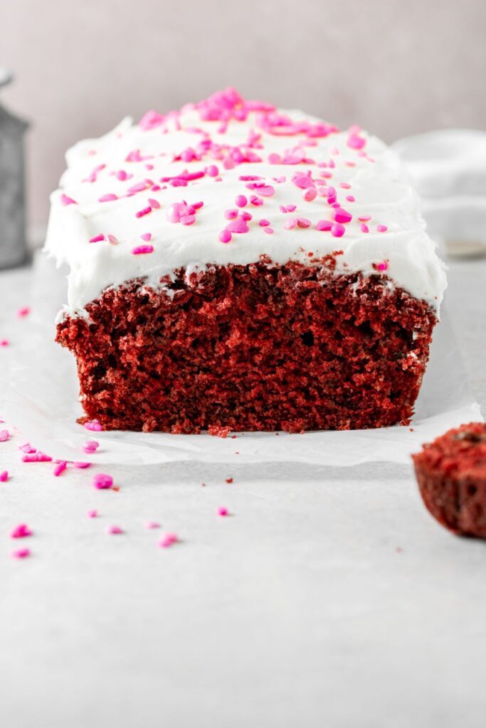 Red velvet loaf that's bright red and covered in cream cheese icing and pink sprinkles.
