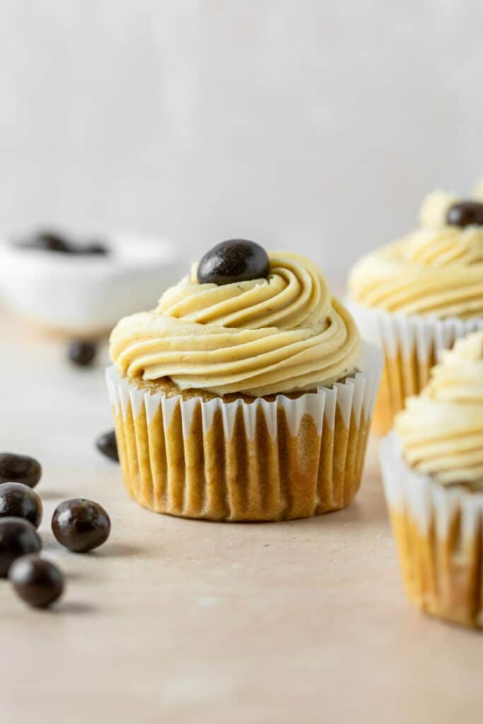 Homemade coffee cupcakes with swirled coffee frosting on top and chocolate beans on the side.