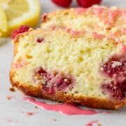 Lemon raspberry cake slices with pink icing and red raspberries in the background.
