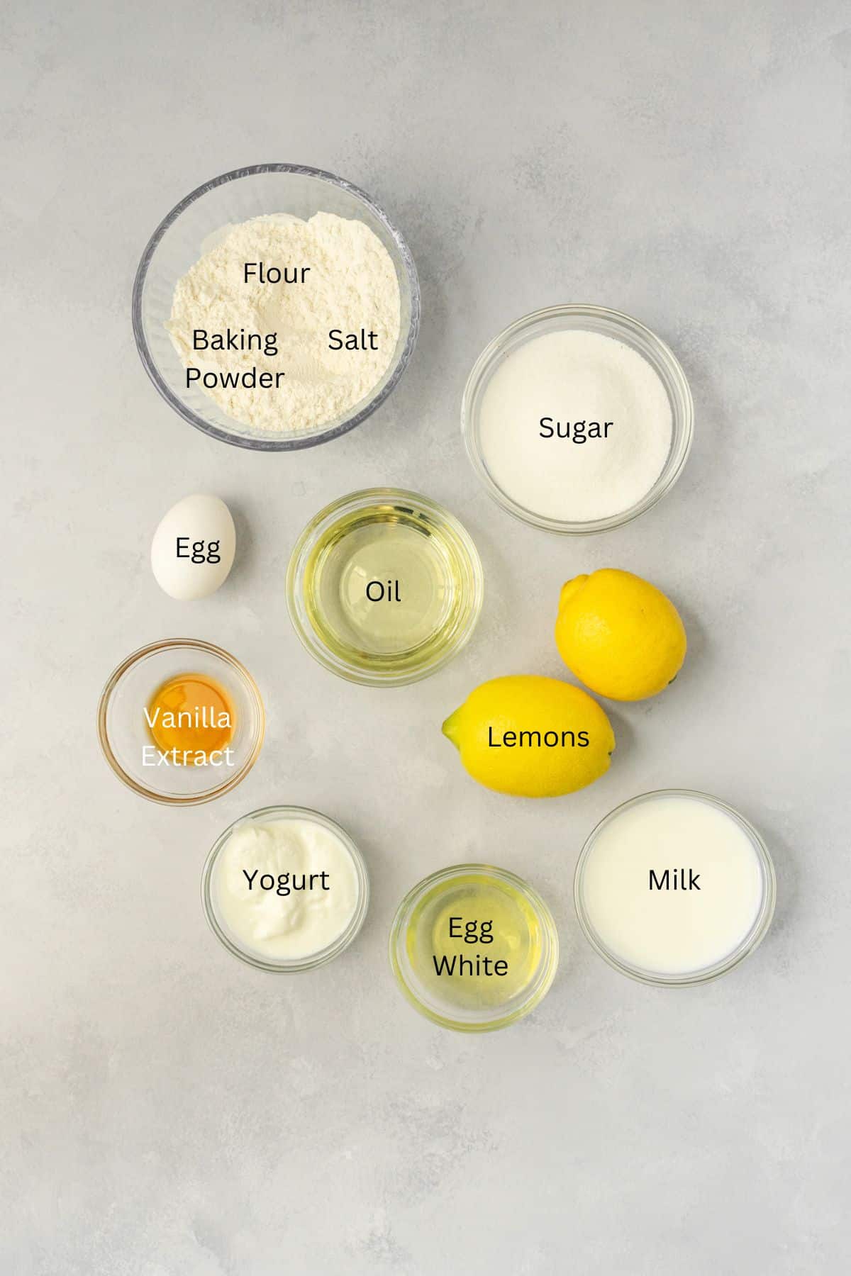 Ingredients in lemon cupcakes: flour, baking powder, salt, sugar, eggs, lemons, oil, vanilla, yogurt, and milk.