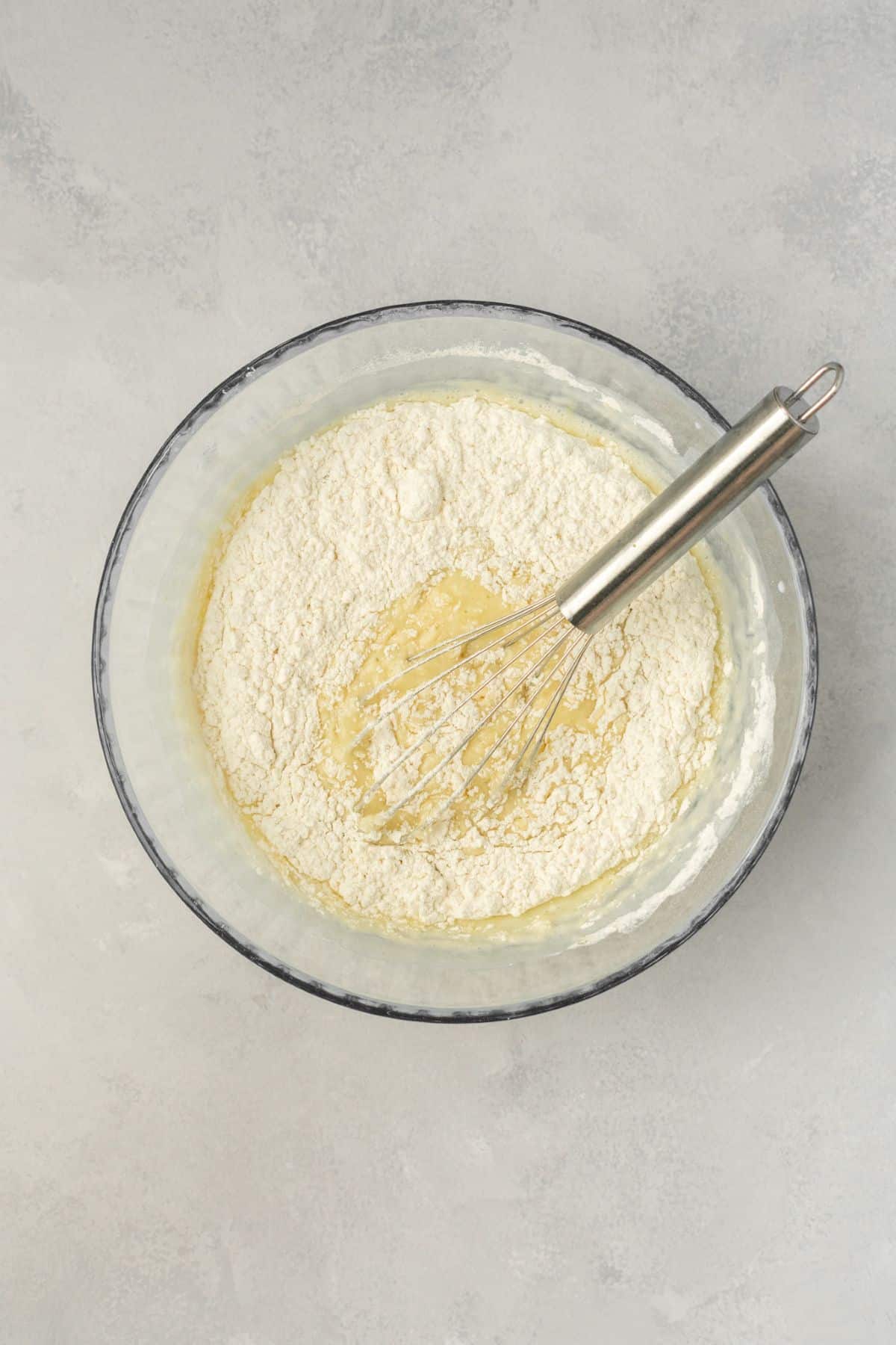 Whisking in the dry ingredients into the bowl of mixed wet ingredients to create a batter.