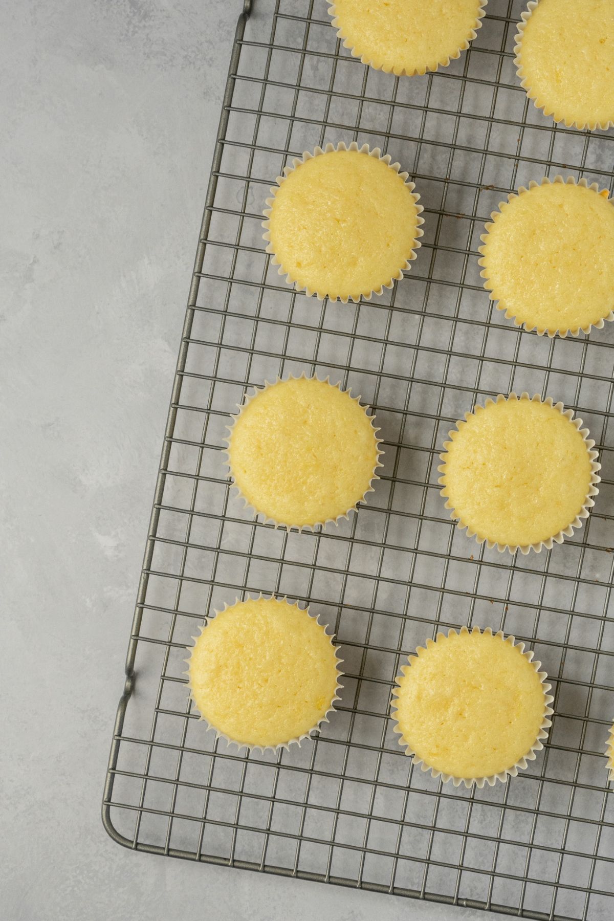Baked lemon cupcakes cooling on a wired rack.