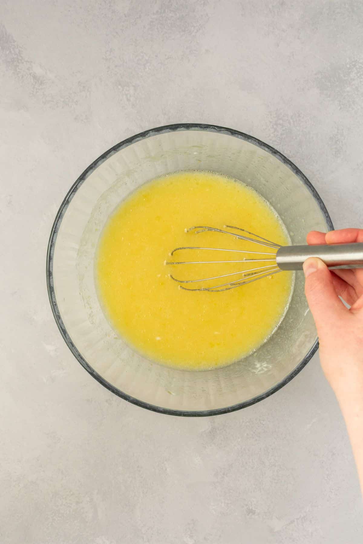 Whisking together eggs, sugar, and lemon juice in a glass bowl.