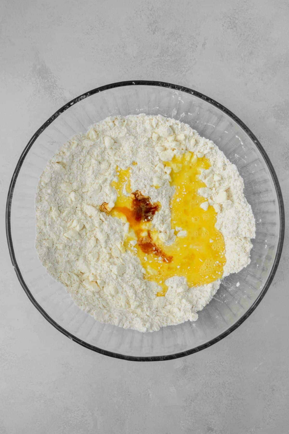 A beaten egg and vanilla extract added to a large glass bowl that's filled with flour.