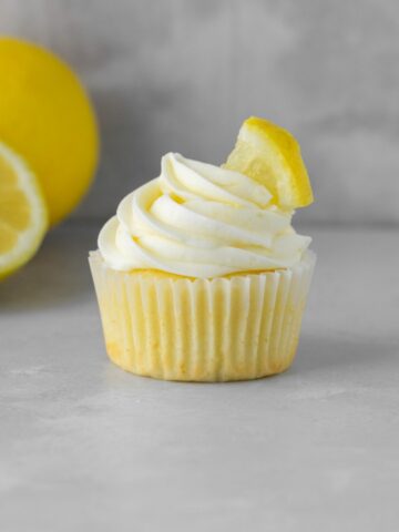 A lemon cupcake with lemon cream cheese frosting on top and a lemon slice.