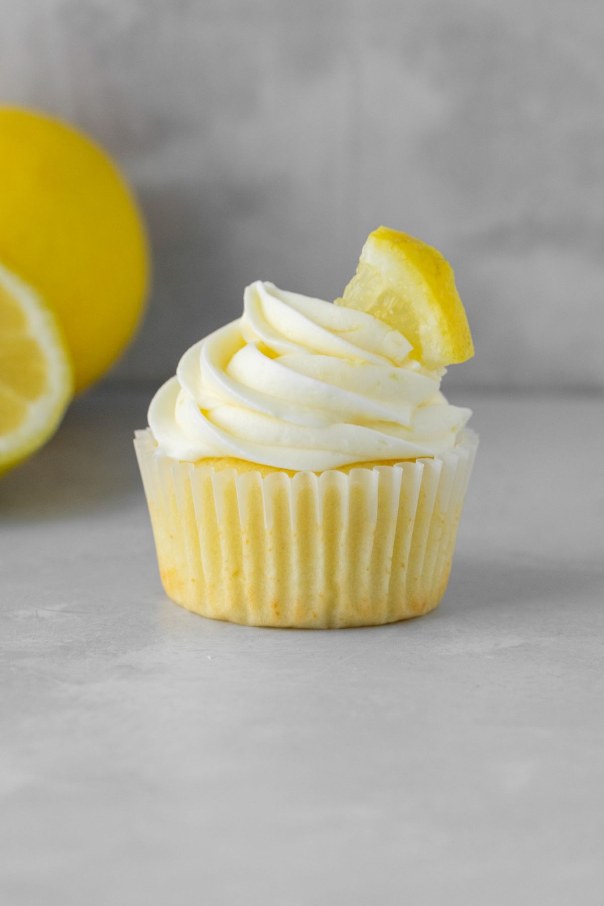 A lemon cupcake with lemon cream cheese frosting on top and a lemon slice.