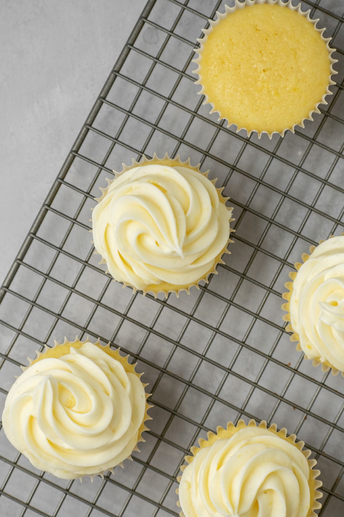 Cupcakes on top of a wire rack with lemon cream cheese frosting on top.