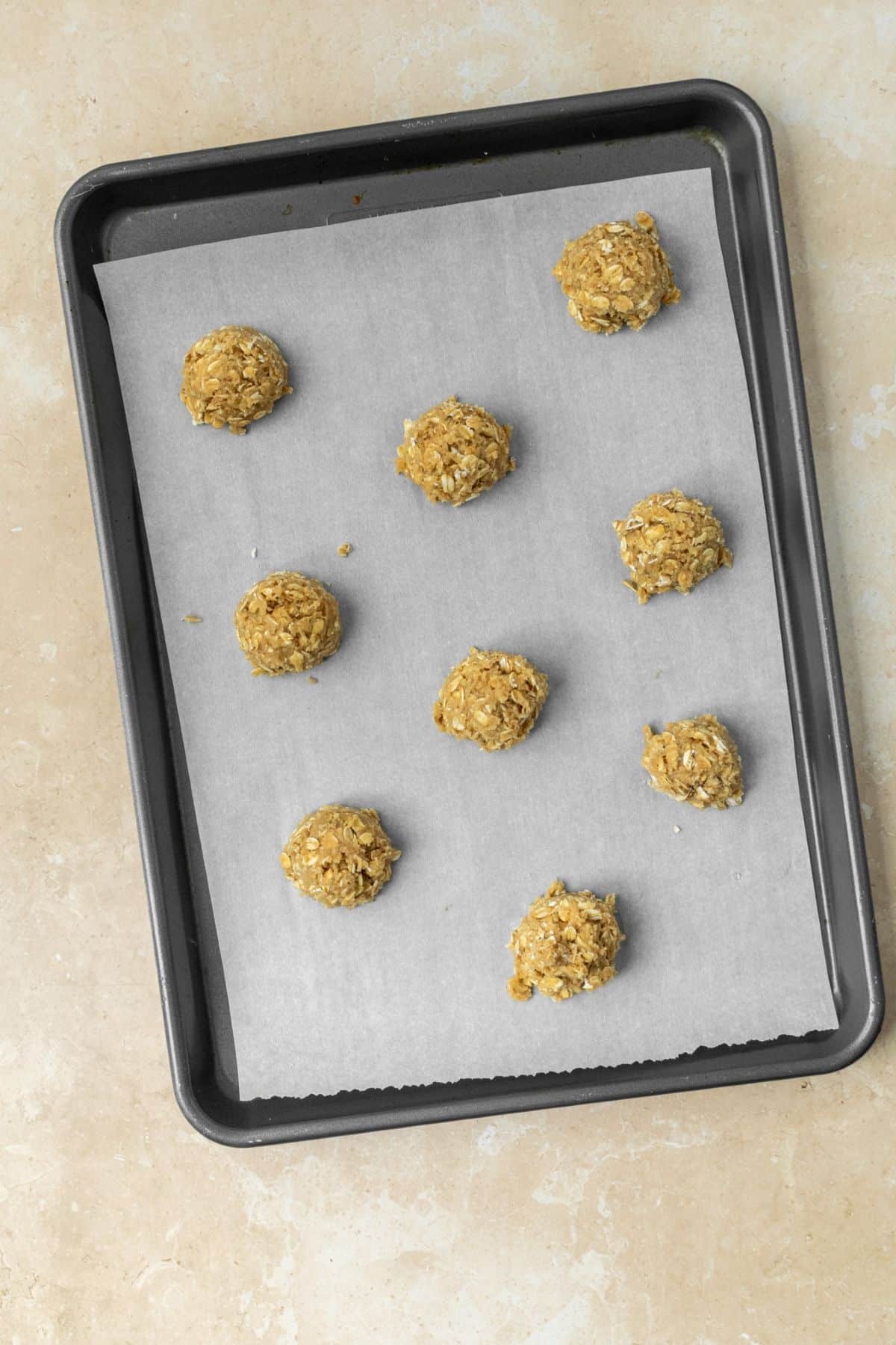 Oatmeal cookie dough balls on a parchment paper lined baking pan.
