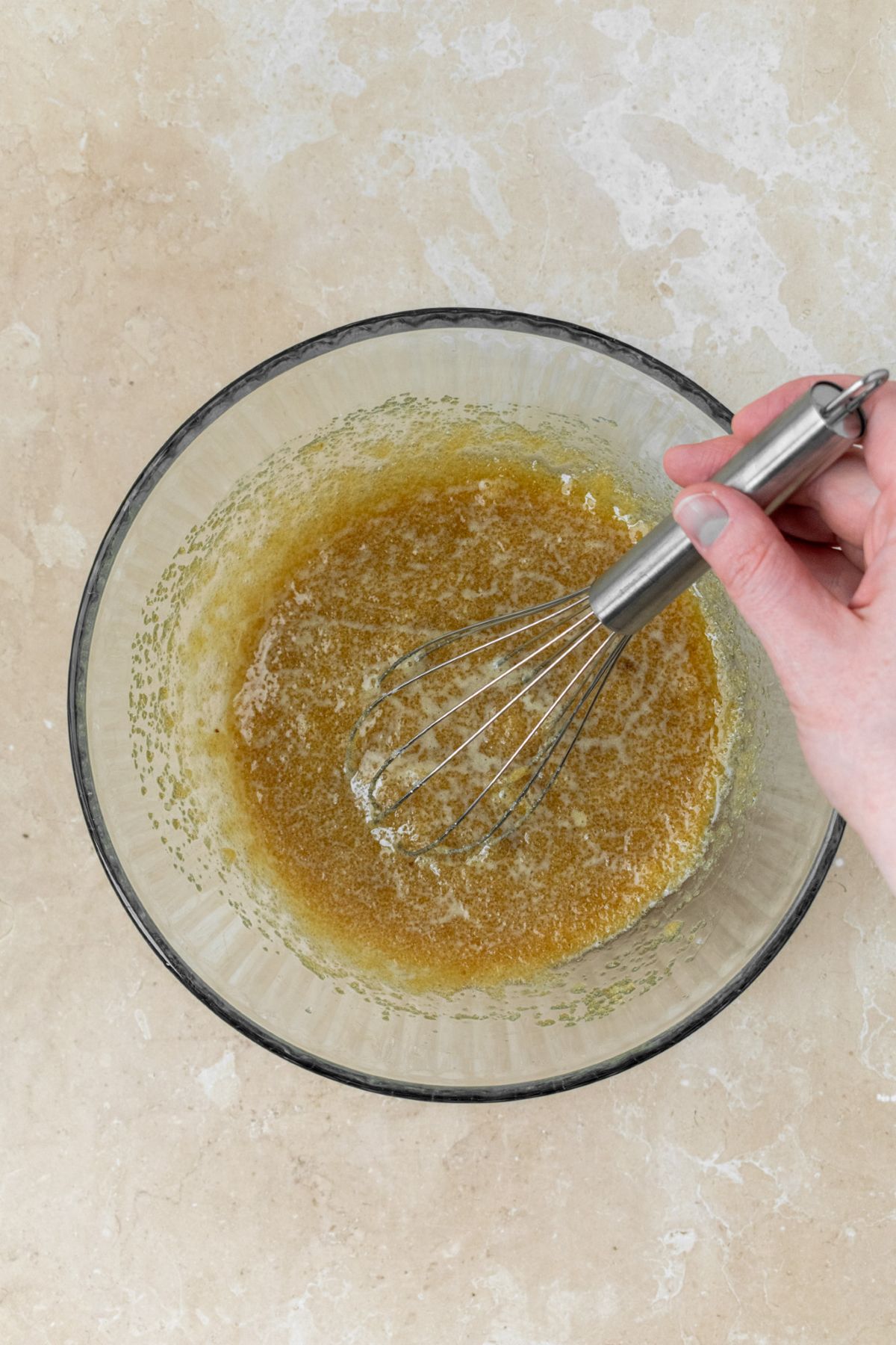 Melted butter and sugars whisked together in a glass bowl.