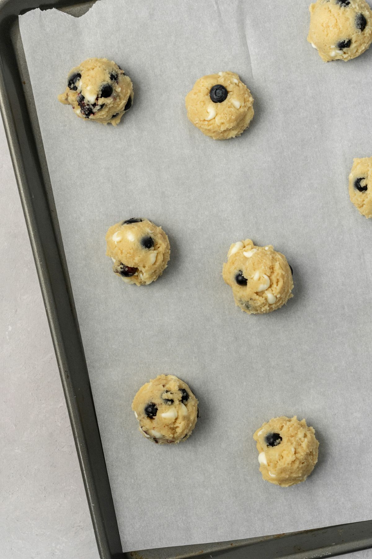 White chocolate blueberry cookie dough balls on a parchment paper lined baking sheet.