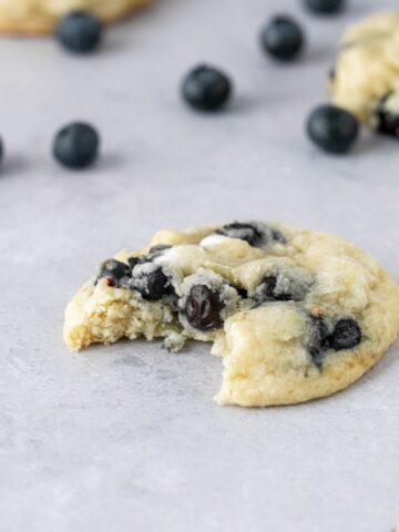 A bite taken out of a chewy blueberry white chocolate cookie.