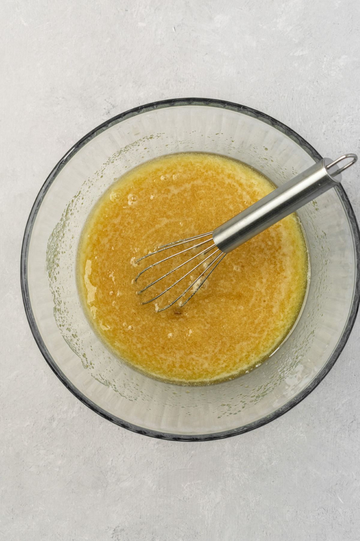 A large glass bowl with melted butter and sugar whisked together.