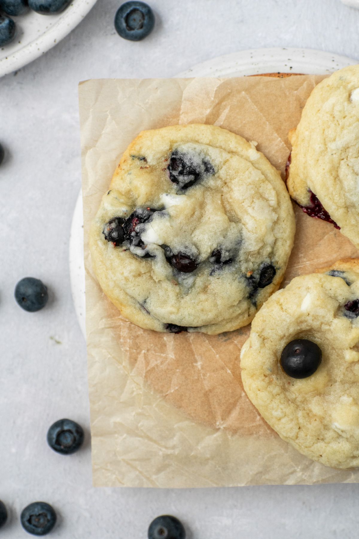 Blueberry white chocolate cookies on a white plate with fresh blueberries all around.