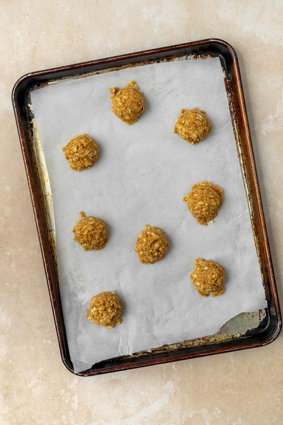 Eight cookie dough balls on a parchment paper lined baking sheet.