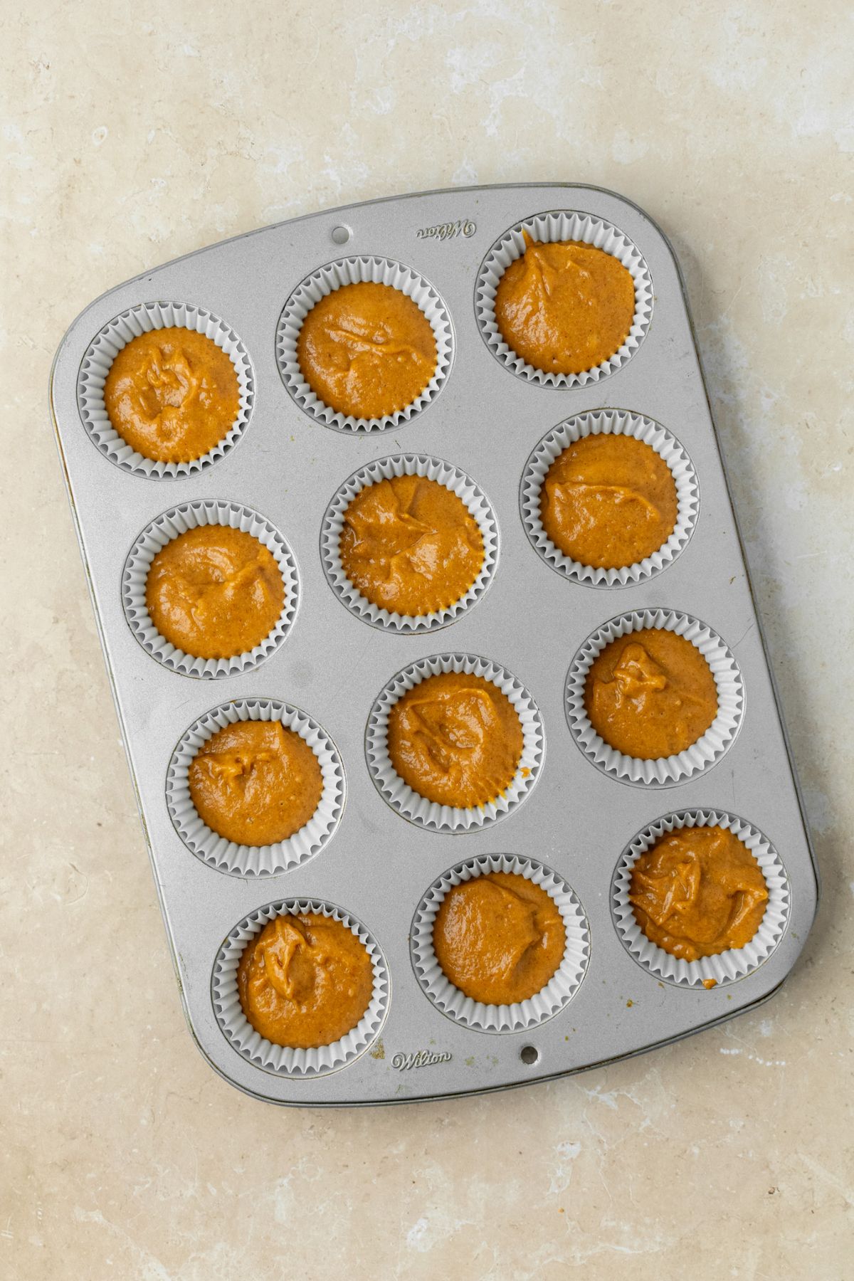 Pumpkin cupcake batter in a muffin pan.