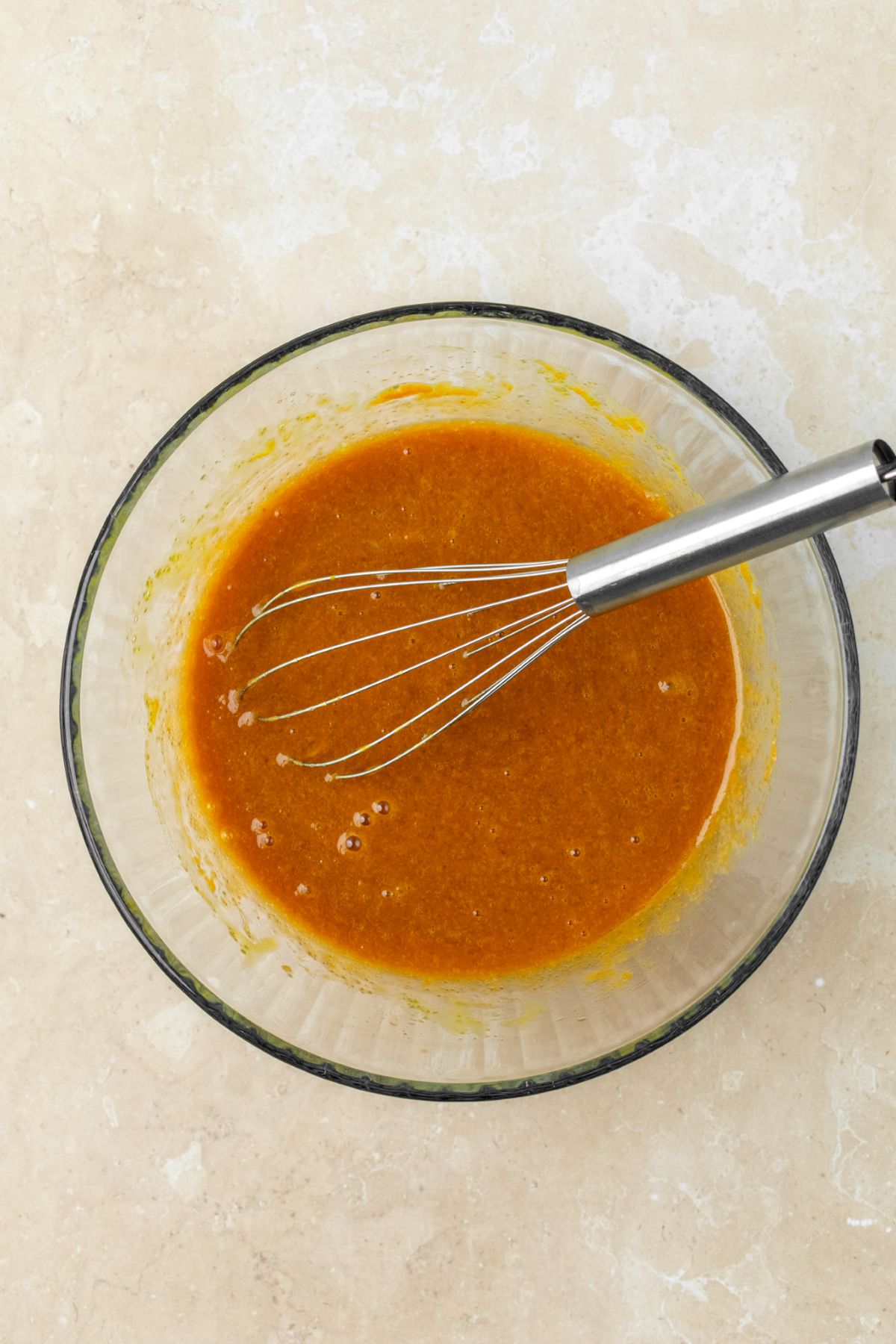 Wet ingredients for pumpkin cupcakes in a glass bowl with a whisk.