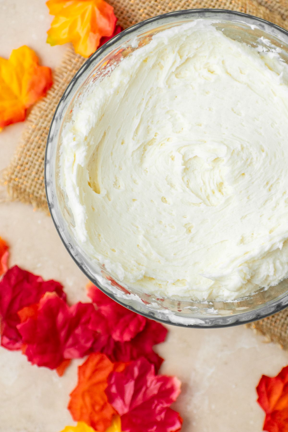 Maple frosting in a bowl with red and orange maple leaves all around it.
