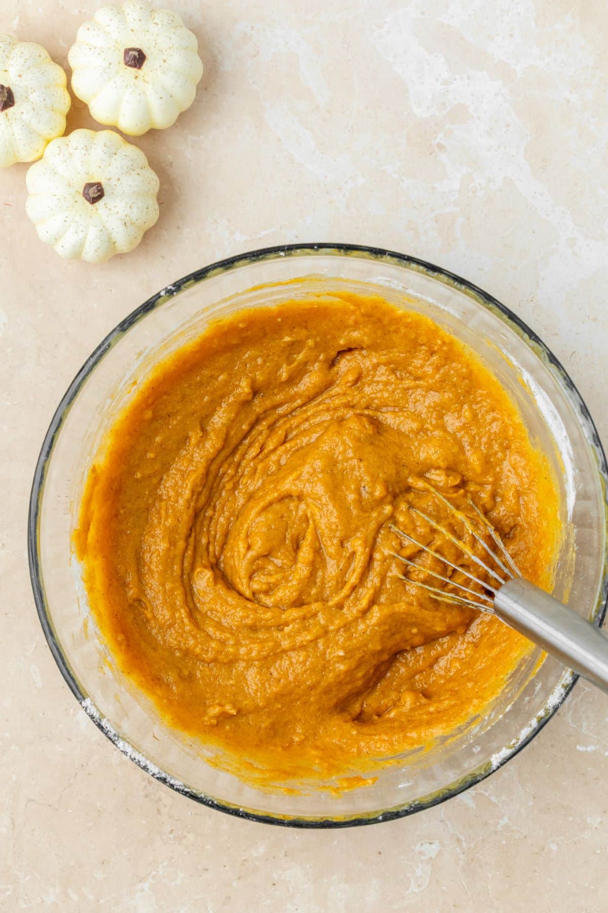 A small batch of pumpkin cake batter whisked together in a glass bowl.