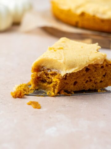A slice of moist pumpkin cake topped with frosting and a bite taken out of it.