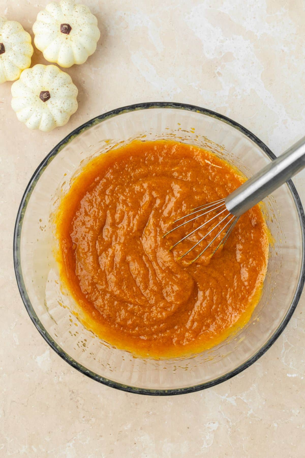 Pumpkin puree and other wet ingredients whisked together in a large glass bowl.