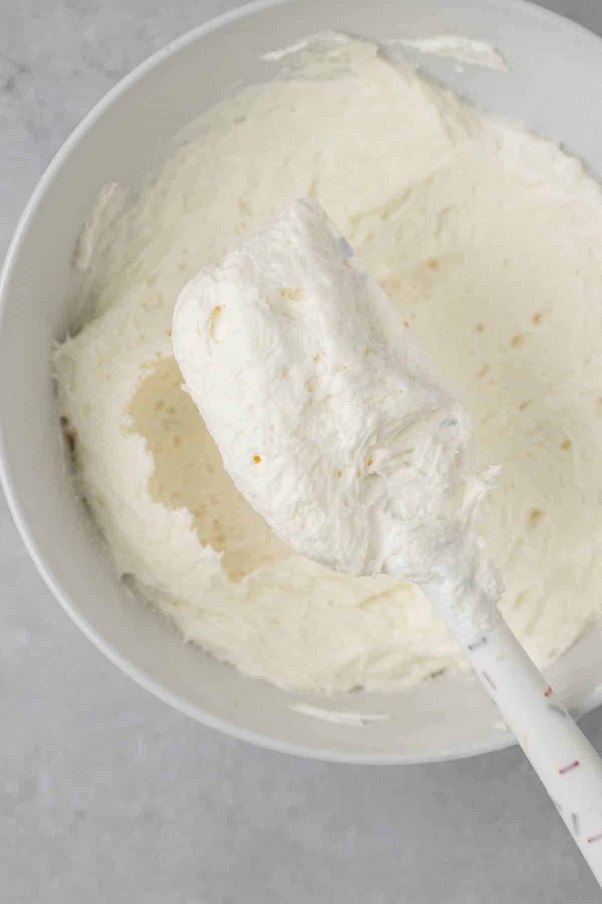 Marshmallow fluff frosting in a bowl and on a rubber spatula.