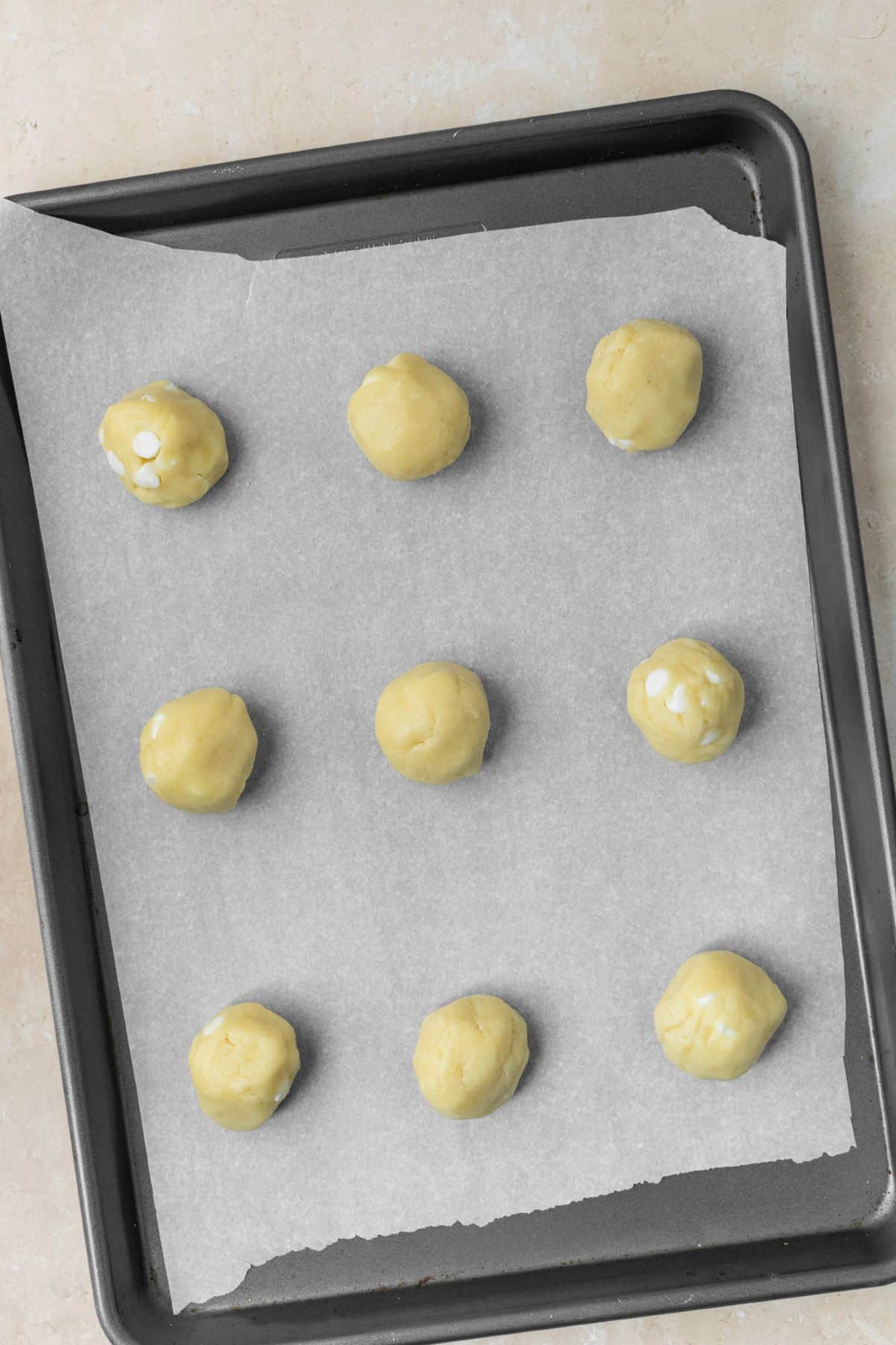 Baking sheet lined with parchment paper with 9 sugar cookie dough balls on top.