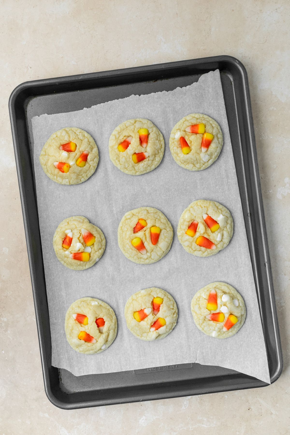 Nine candy corn sugar cookies on a baking sheet.
