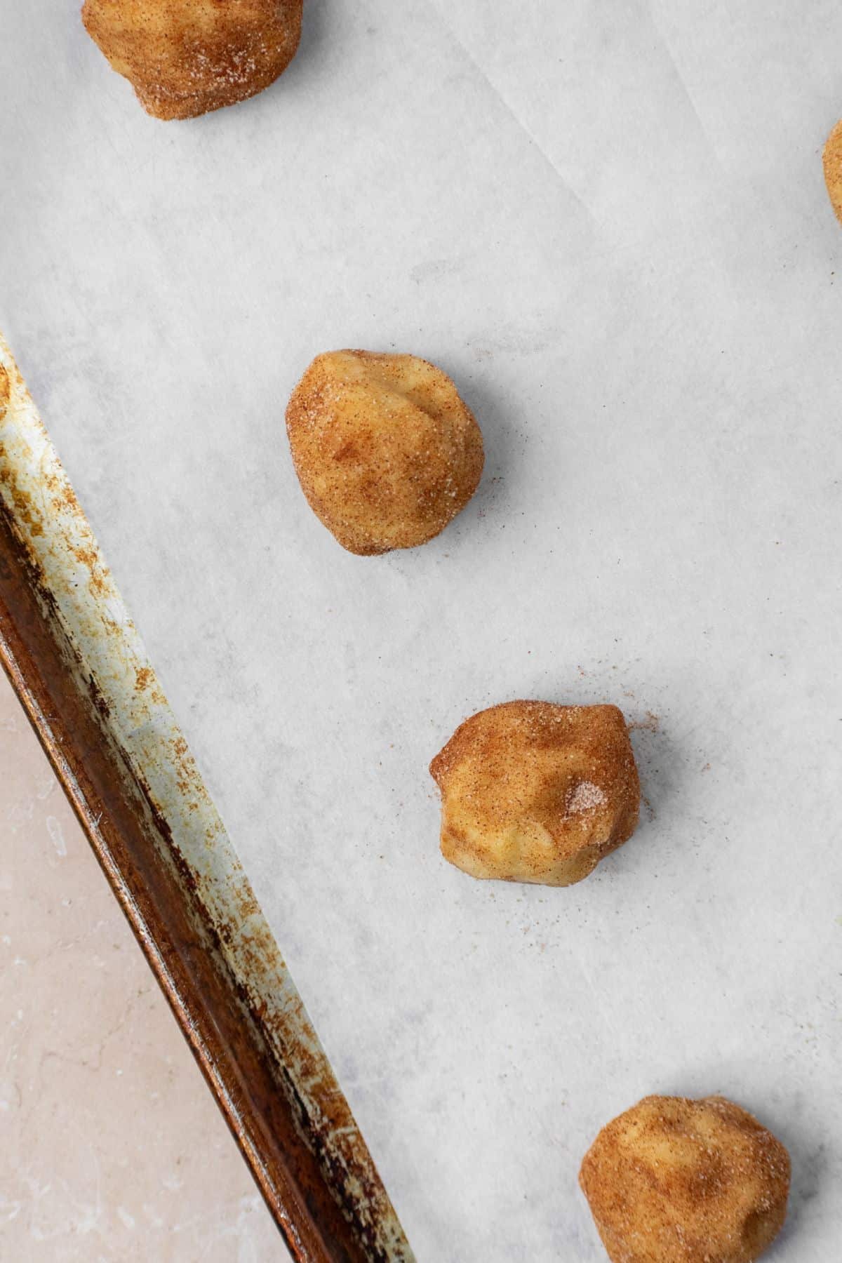 Snickerdoodle cookie dough balls on a parchment paper lined baking sheet.
