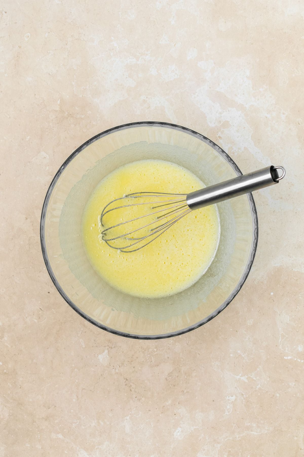 Eggs and sugar whisked together in a glass bowl.