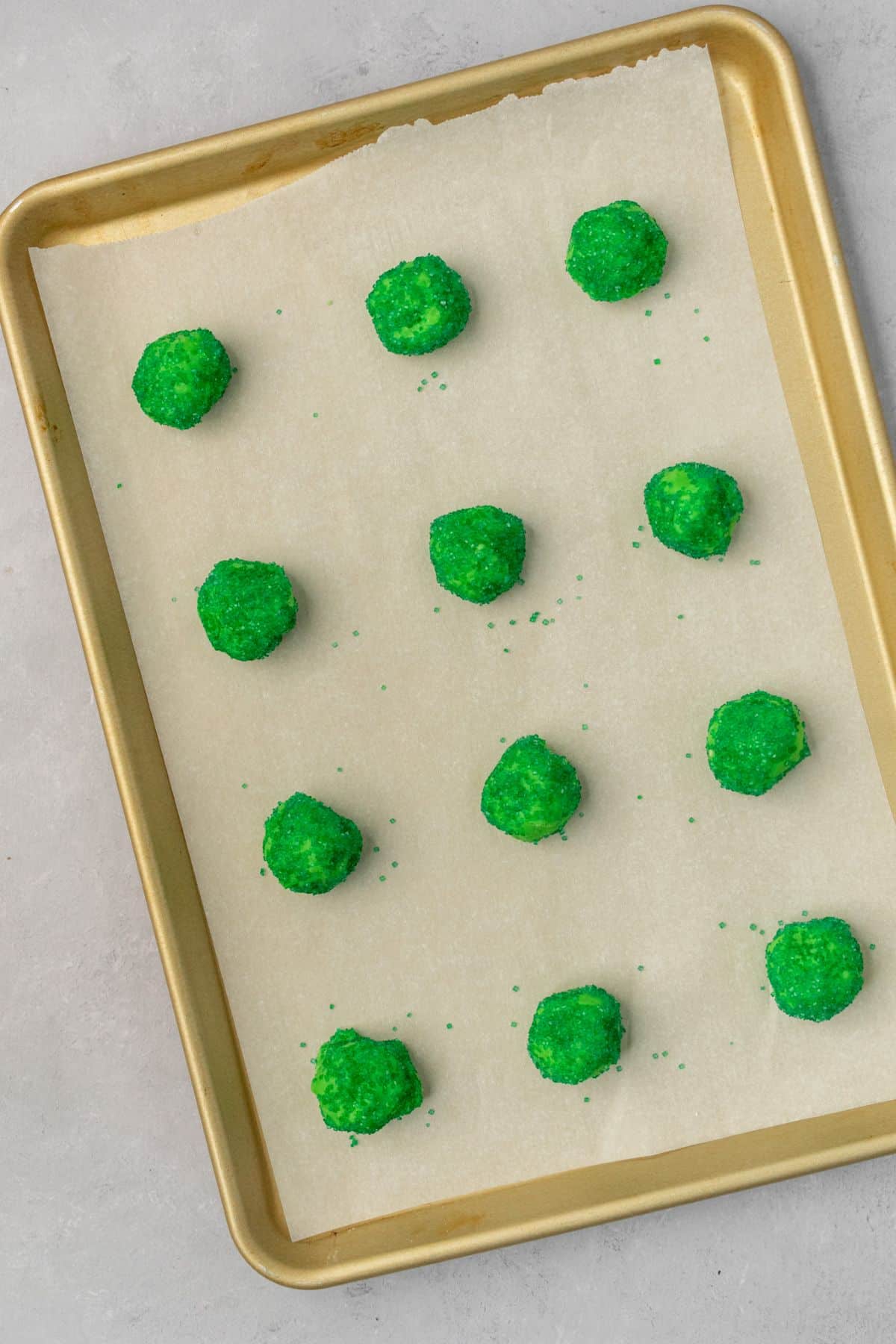 Twelve cookie dough balls on a parchment paper lined baking sheet.