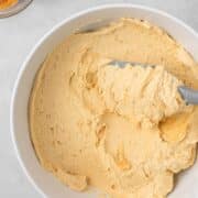 Creamy peanut butter frosting in a bowl with a small bowl of peanut butter off to the side.