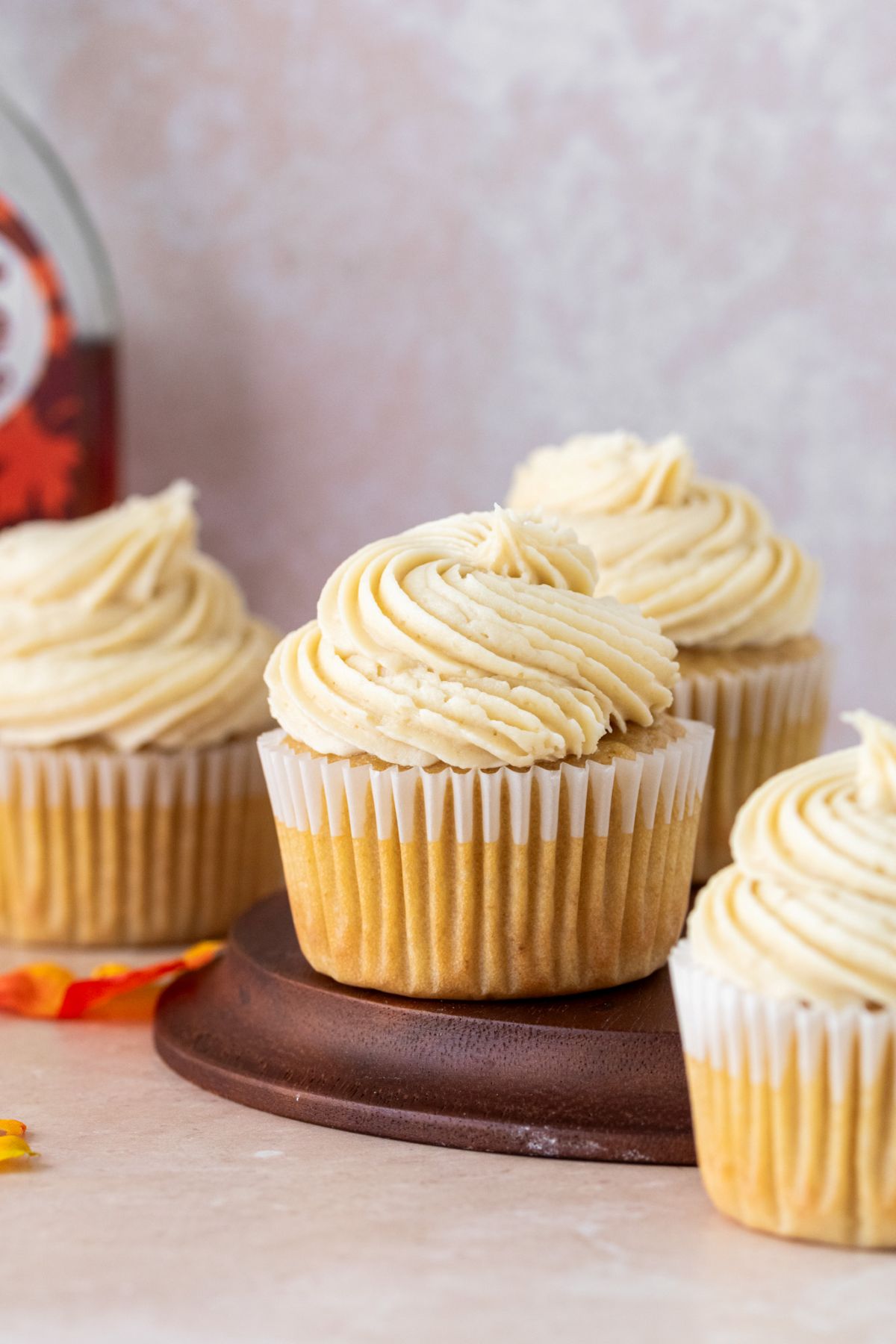 Maple cupcakes sitting on a brown plate with a bottle of maple syrup in the background.