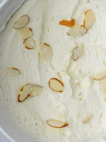 Almond buttercream in a white bowl with thinly sliced almond pieces on top.