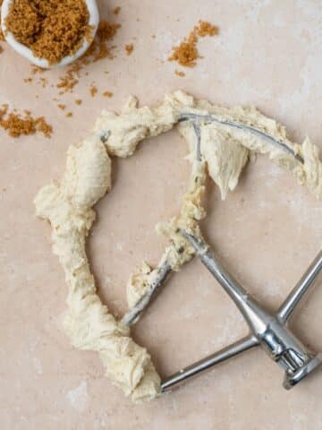 Brown sugar buttercream on a paddle attachment with brown sugar in a small bowl.