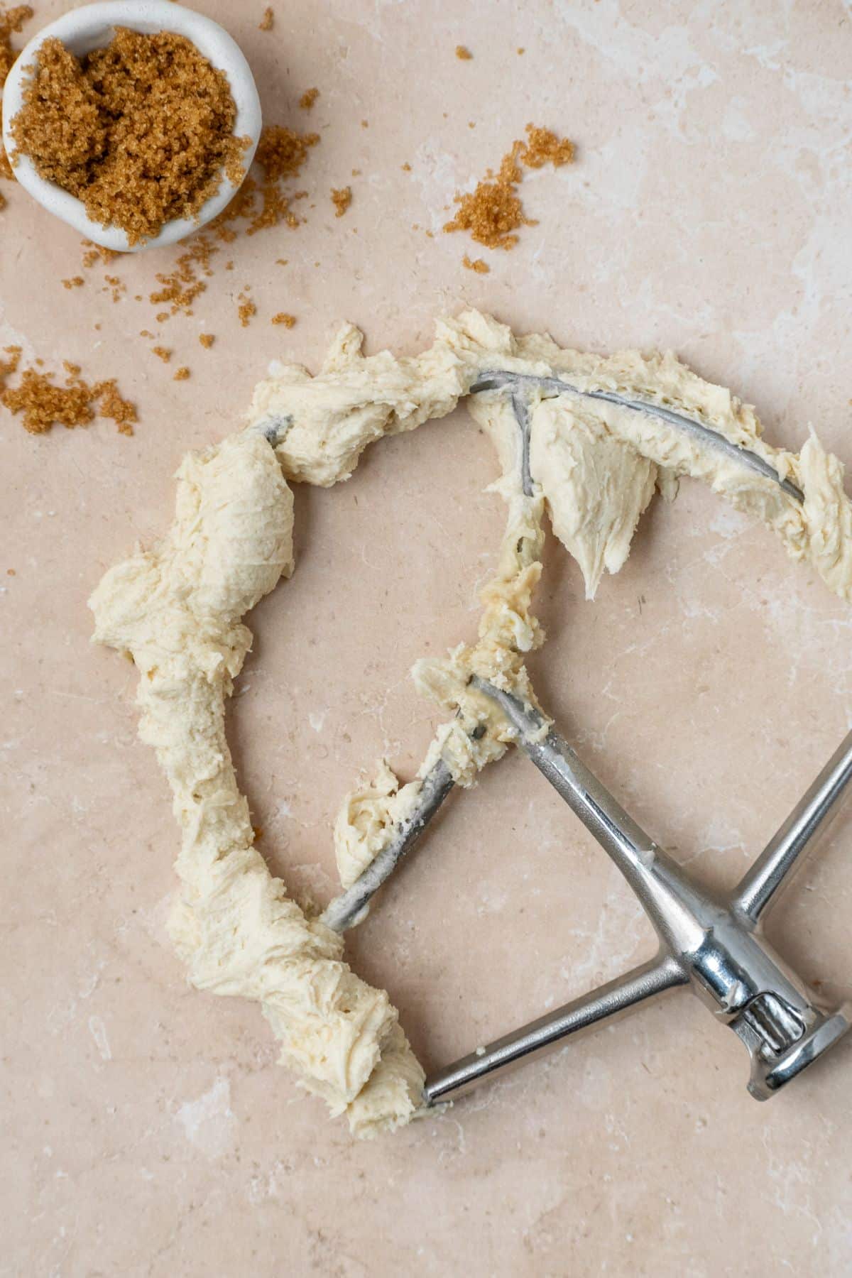 Brown sugar buttercream on a paddle attachment with brown sugar in a small bowl.
