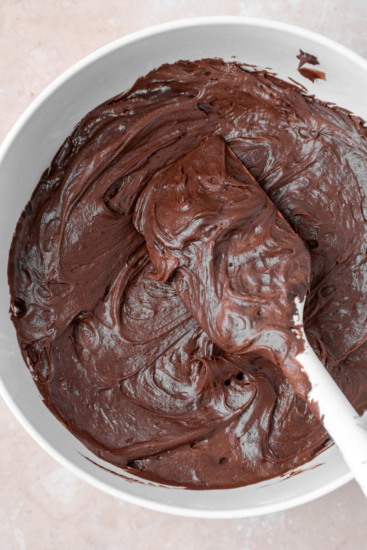 Chocolate cream cheese frosting in a bowl with a silicone spatula.
